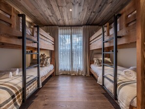 A room with bunk beds, wooden floors, and a window with curtains. - Luxury 4-bedroom apartment with 5* concierge, mountain view (Les Allues)