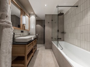 Ein modernes Badezimmer mit einem Holz-Waschtisch, zwei Waschbecken, einer großen Badewanne und einer gläsernen Dusche.