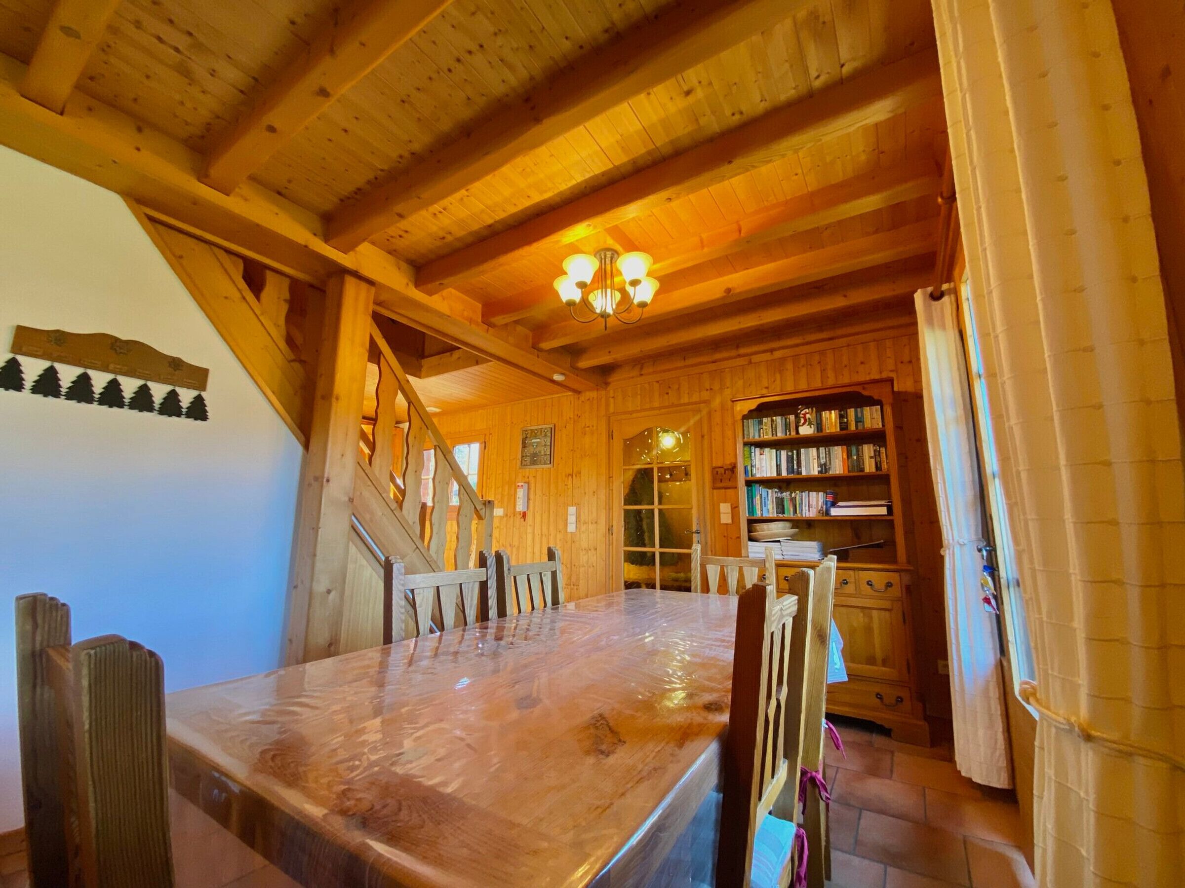 Een houten interieur met een eettafel, stoelen, een trap, een boekenplank en een kroonluchter.