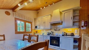 A compact kitchen with white cabinets, a microwave, an oven, and a sink. There is a window above the sink, and wooden chairs are placed around a table. - Cozy duplex for 6 in Morillon with parking (Morillon Village)