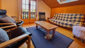 A cozy room with a wooden ceiling, a checkered sofa, a leather chair, a wooden table, and a large window with a view. - Cozy duplex for 6 in Morillon with parking (Morillon Village)