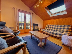 Ein gemütliches Zimmer mit Holzboden, einem karierten Sofa, einem Ledersessel, einem Holztisch und einem großen Fenster mit Blick.