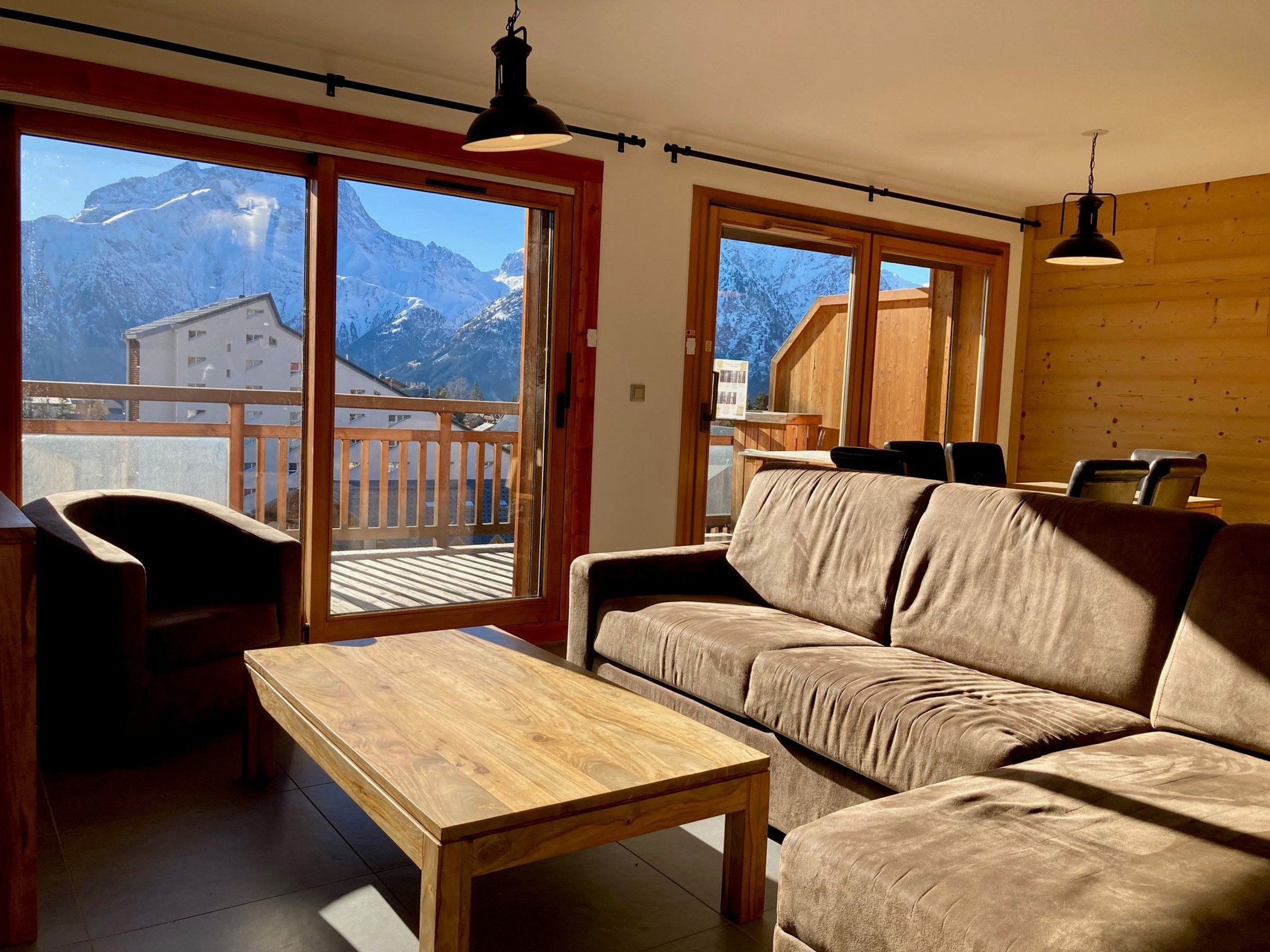 Un salón acogedor con un sofá de madera, una mesa de centro de madera y vistas a montañas nevadas a través de amplios ventanales.