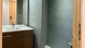 A modern bathroom with dark grey tiles, a wooden door, and a white sink with a wooden cabinet.