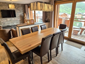Una cocina moderna con una mesa y sillas de madera, una pared de piedra y un ventanal con vistas a un pueblo en la montaña.