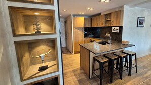 Eine moderne Küche mit Holzschränken, einer zentralen Kochinsel mit Barhocker und Einbaustrahlern.