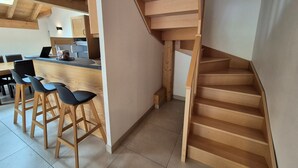 A modern kitchen with wooden accents, a dining area with bar stools, and a wooden staircase. - Bright duplex apt 8 people, 250m from slopes, pets allowed (Les Deux Alpes)