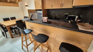 A modern kitchen with wooden cabinets, a black countertop, and bar stools. - Bright duplex apt 8 people, 250m from slopes, pets allowed (Les Deux Alpes)