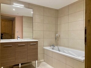 Een moderne badkamer met een grote spiegel, een wastafel met drie lades, een bad en betegelde wanden.