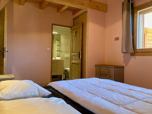 Een slaapkamer met twee bedden, een houten dressoir en een zichtbare badkamer door een geopende deur.