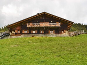 A wooden chalet with a balcony, stone foundation, and a grassy foreground.