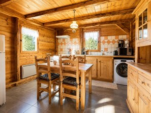 A wooden cabin interior with a dining table, chairs, a kitchen area with appliances, and a washing machine.