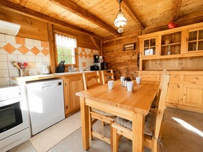 A wooden interior with a kitchen area, a dining table with chairs, and a built-in cabinet.