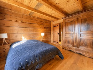 A wooden-paneled room with a bed, a wardrobe, and a nightstand with a lamp.