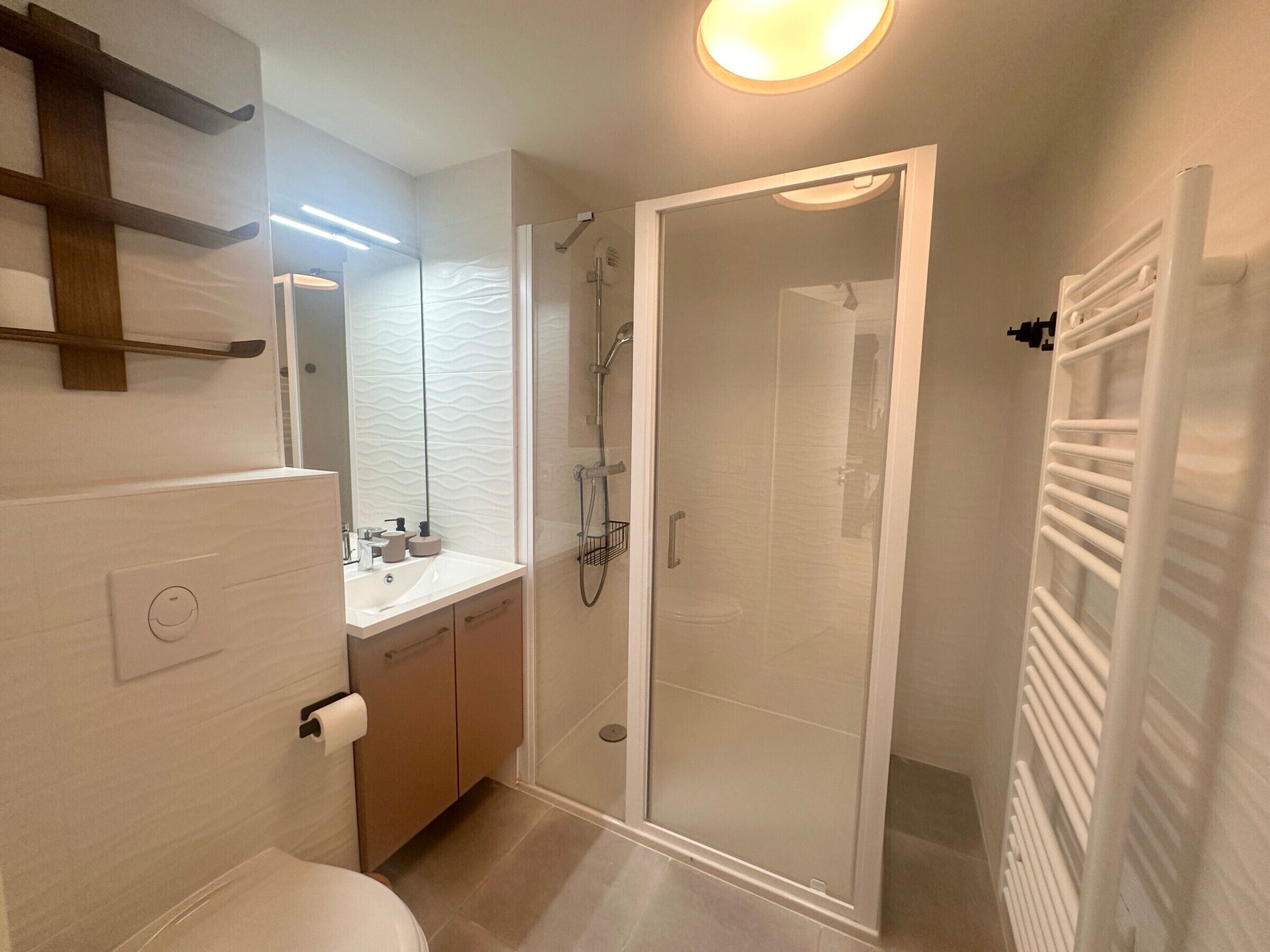 A modern bathroom with a glass-enclosed shower, a wooden vanity, and a towel rack.