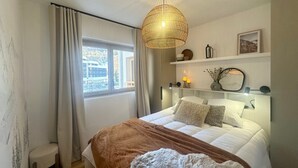 A bedroom with a bed, a window, a bedside lamp, a shelf with decorative items, and a hanging light fixture. - Apartment Vars, 2 bedrooms, 5 persons (Vars)