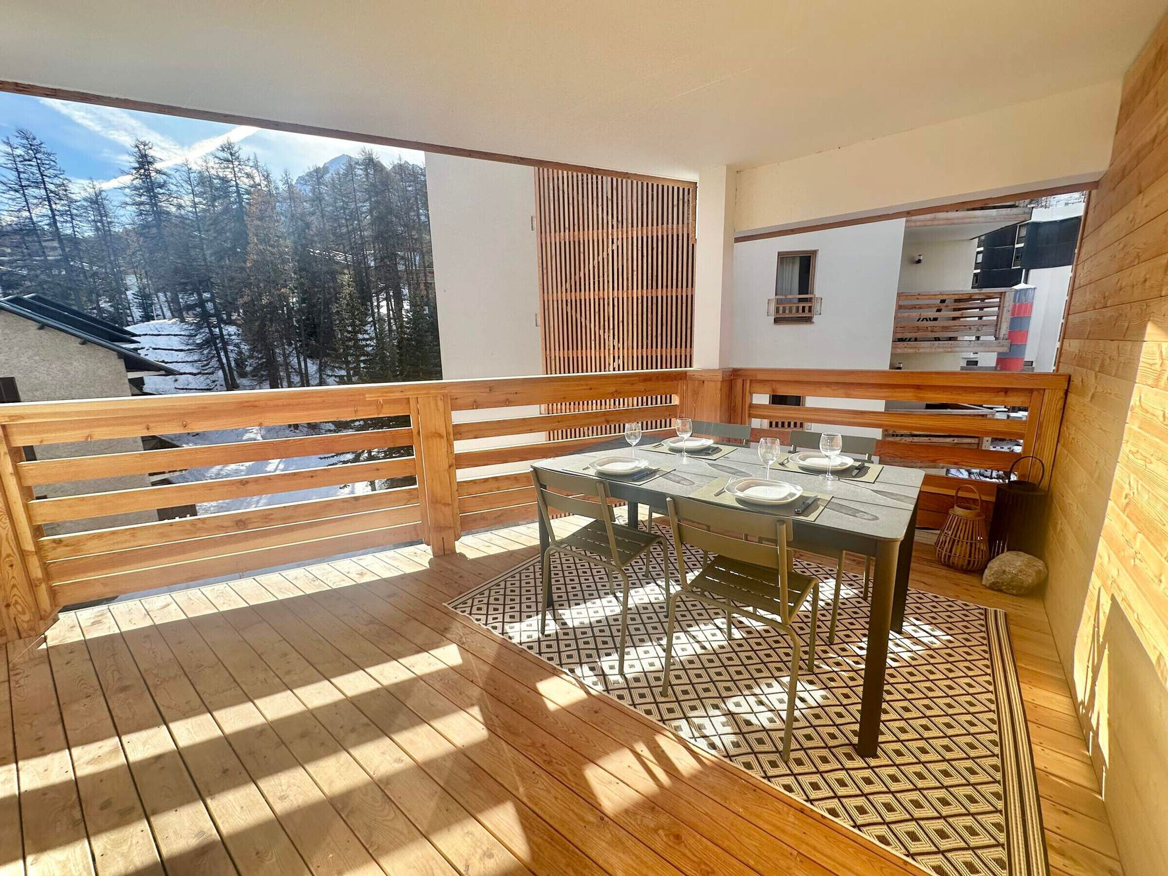Une terrasse en bois avec une table dressée pour deux personnes, donnant sur une forêt enneigée.