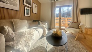 A modern living room with a sofa, a round coffee table with candles, and a large window with a view of trees. - Apartment Vars, 2 bedrooms, 5 persons (Vars)