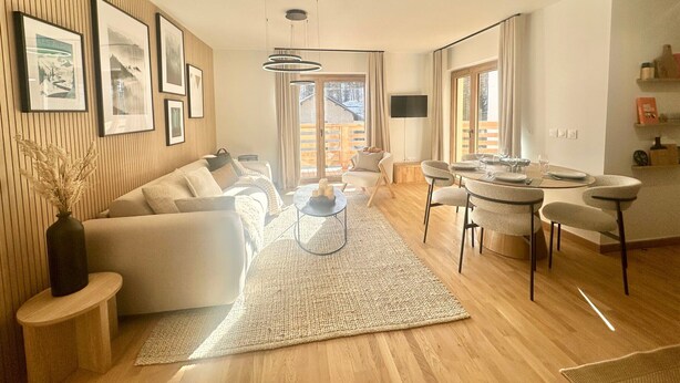 A modern living room with a sofa, coffee table, and dining area with chairs and a table set for two. - Apartment Vars, 2 bedrooms, 5 persons (Vars)