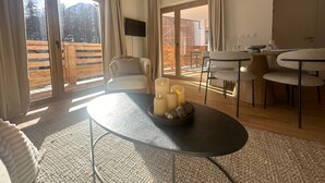 A modern living room with a glass door leading to a balcony, a round table with candles, and a seating area with chairs. - Apartment Vars, 2 bedrooms, 5 persons (Vars)