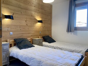 A room with two beds, wooden headboard, bedside tables, and a window with curtains.