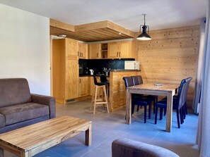 A compact living space with a kitchenette, wooden dining table, and a sofa.