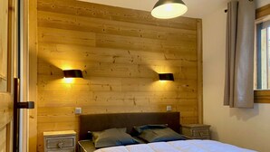 Un dormitorio con cabecera de madera, dos lámparas de noche, una cama con ropa blanca y una mesita de noche con cajón.