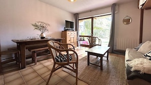 A cozy living room with a dining area, a television, and a large window offering a view of the outdoors.