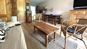 A cozy living room with a wooden dining table, wicker chairs, a sofa, and a television.