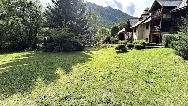 A lodge with a wooden exterior, surrounded by lush greenery and mountains in the background.