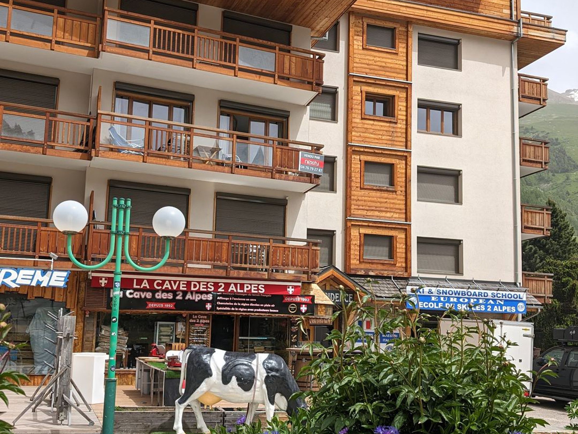 A multi-story building with wooden balconies and a sign for "La Cave des 2 Alpes".