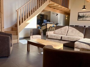 A modern living room with a wooden staircase, a sofa, a coffee table, and a kitchen area in the background.