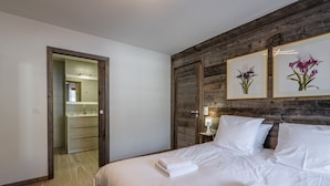 Un dormitorio con una pared de acento de madera, una cama con ropa de cama blanca, una mesita de noche y una obra de arte floral enmarcada.