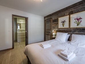 Ein Schlafzimmer mit einer Wand in Holzoptik, einem Bett mit weißer Bettwäsche, einem Nachttisch und einem gerahmten Blumenbild.