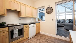 A modern kitchen with wooden cabinets, a dishwasher, and a window overlooking a balcony with a sofa.