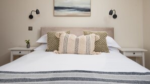 A neatly arranged bedroom with a large bed, two bedside tables, a wall-mounted painting, and two wall sconces.