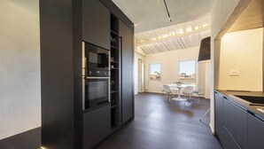Een moderne keuken met donkere kasten, een inbouwoven en een eethoek met een tafel en stoelen.