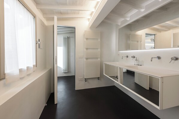 Un baño moderno con un espejo grande, sanitarios blancos y suelo oscuro.