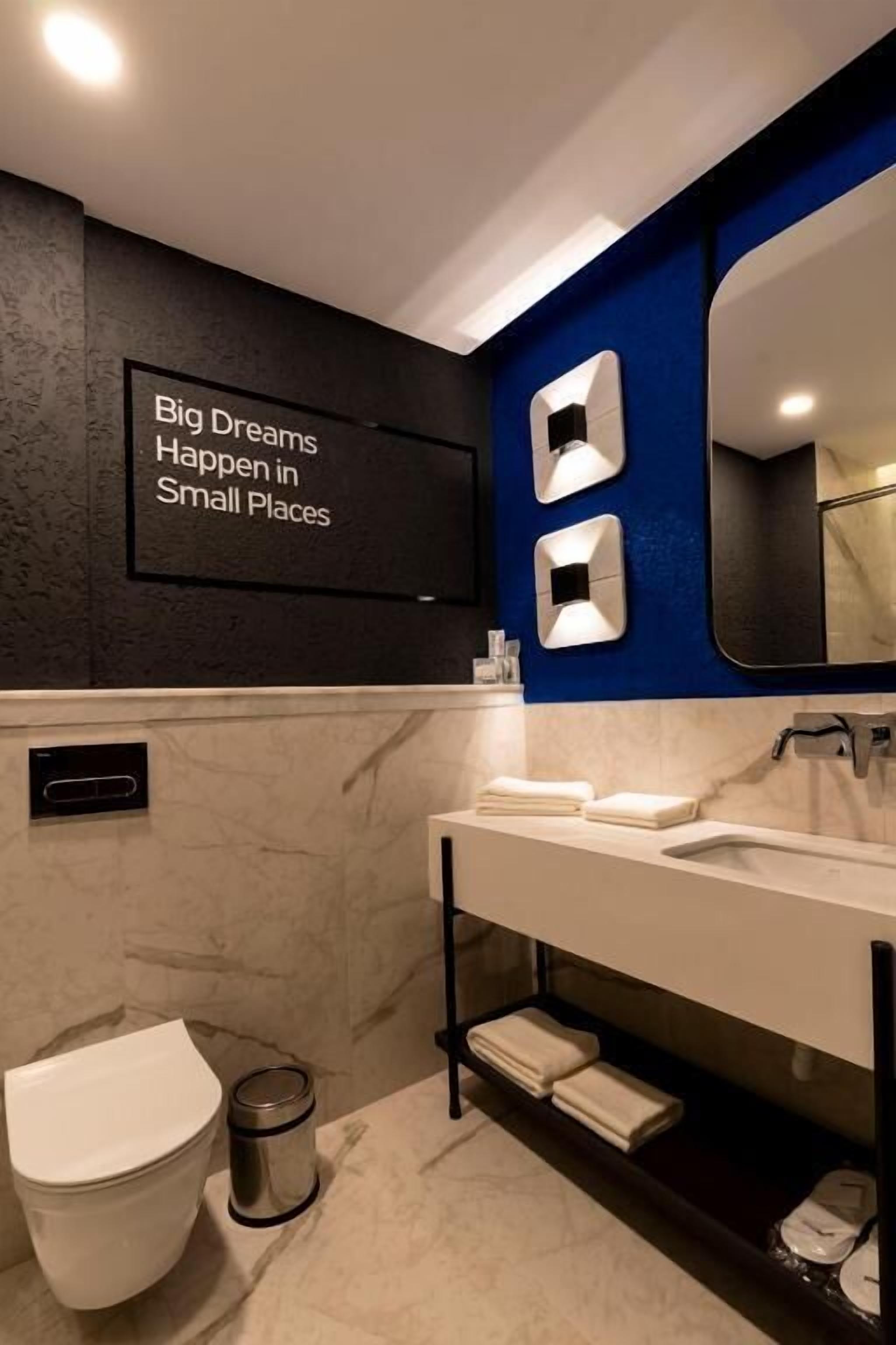 Un baño moderno con suelo de mármol, inodoro blanco, lavabo con espejo y estante con toallas.