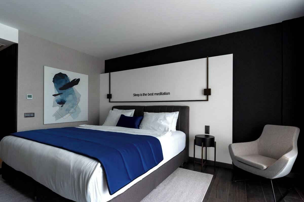 Un dormitorio moderno con una cama grande, una mesita de noche, una silla y una obra de arte colgada en la pared.