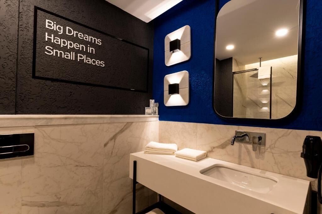 A modern bathroom with a large mirror, a sink, and a wall-mounted light fixture.