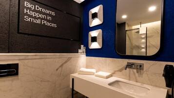 A modern bathroom with a large mirror, a sink, and a wall-mounted light fixture.