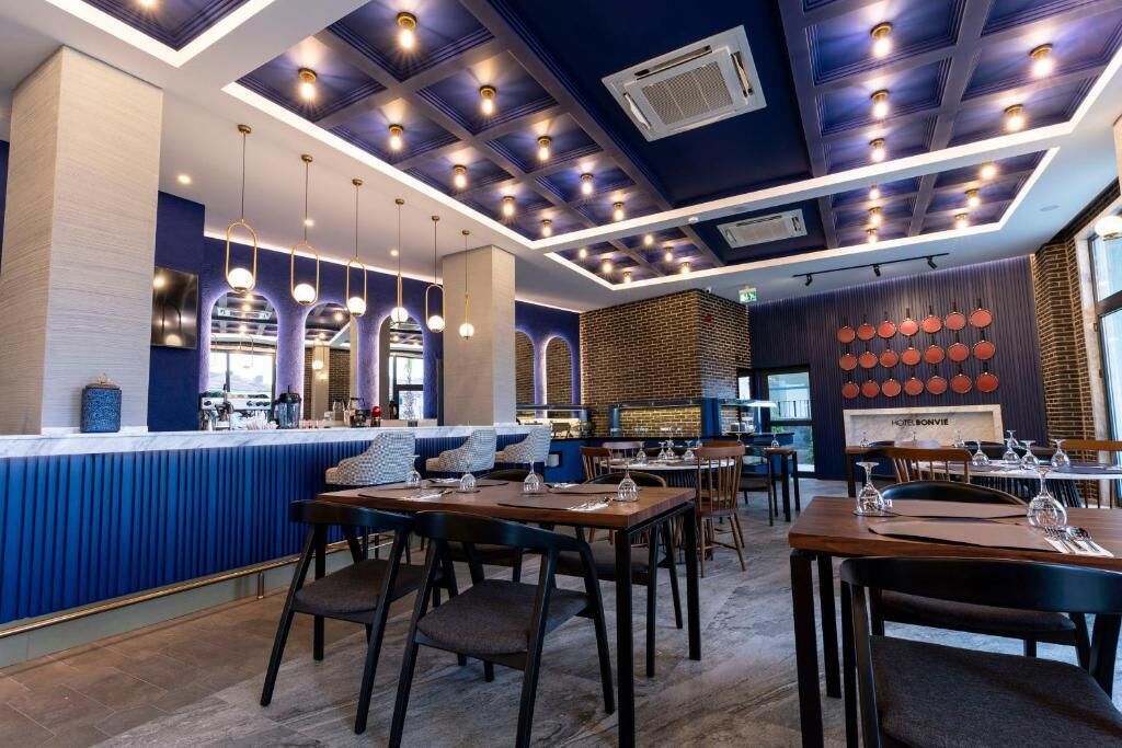 A modern restaurant with a blue and white color scheme, featuring a bar area, dining tables, and hanging pendant lights.