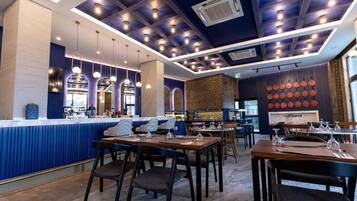 A modern restaurant with a blue and white color scheme, featuring a bar area, dining tables, and hanging pendant lights.