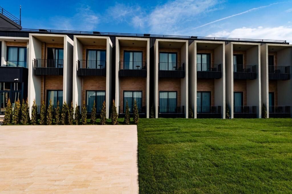 A modern multi-story building with balconies, a paved walkway, and a grassy area.