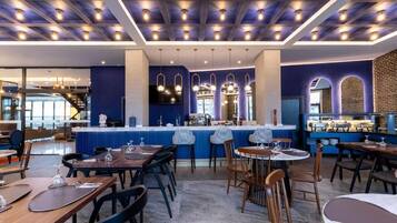 A modern restaurant interior with a bar area, seating arrangements, and a visible kitchen.