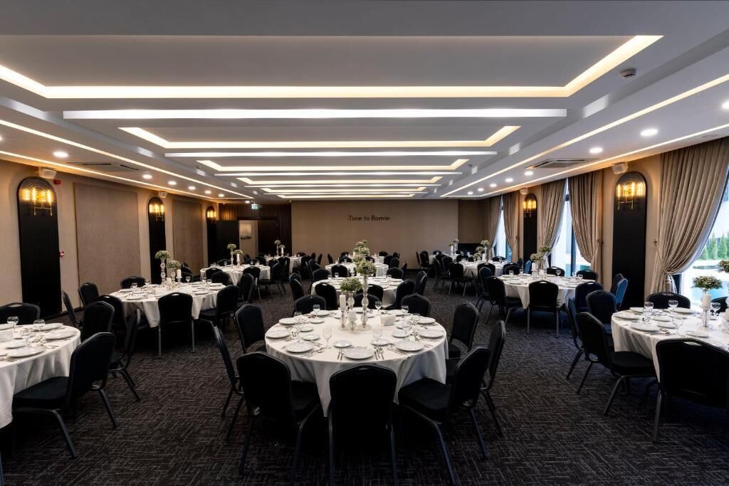 A banquet hall with multiple round tables set for dining, featuring white tablecloths and black chairs.