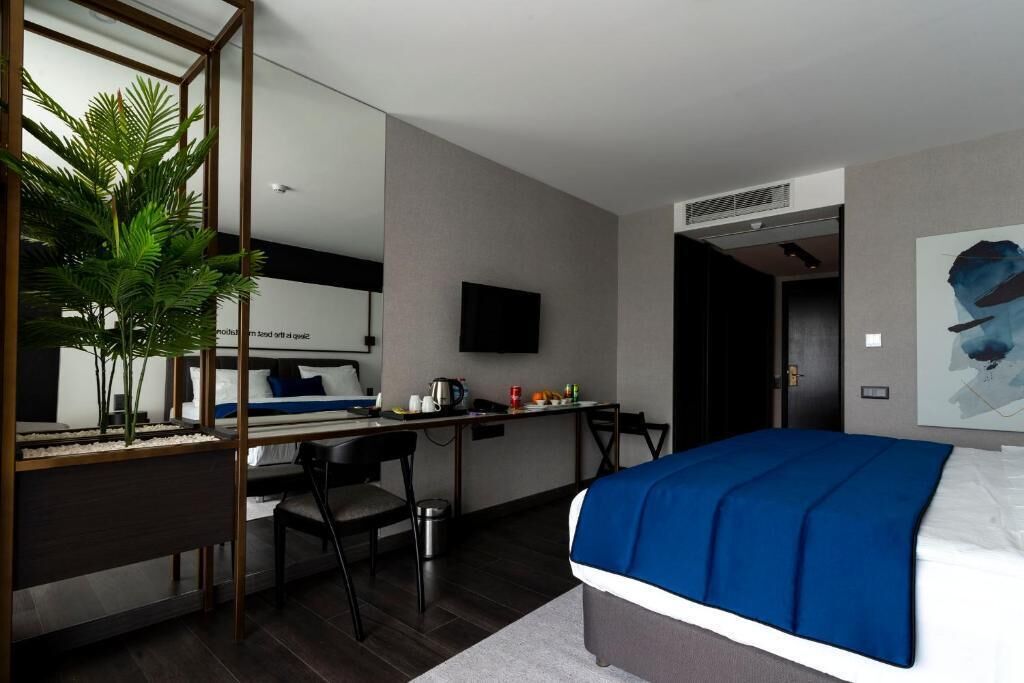 A modern hotel room with a bed, desk, chair, and a large mirror.
