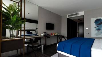 A modern hotel room with a bed, desk, chair, and a large mirror.