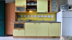 A compact kitchen with a tiled backsplash, wooden cabinets, a built-in microwave, and a small refrigerator.